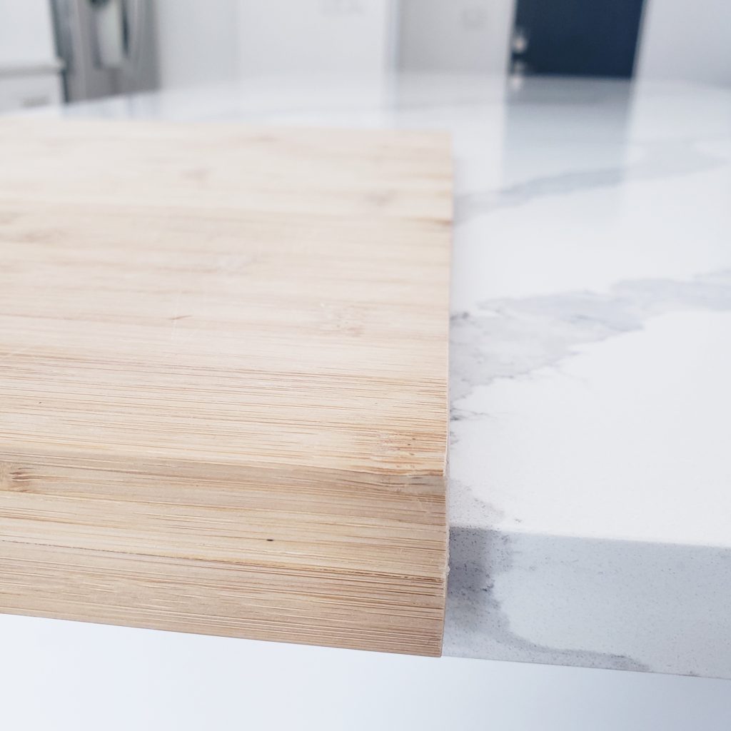 wooden cutting board on grey and white quartz countertop in a minimalist kitchen